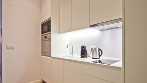 Una cocina moderna con armarios blancos, un lavamanos de acero inoxidable, una cafetera y un hervidor.