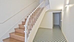 Una escalera de madera con balaustres blancos que conduce a un pasillo con piso estampado.