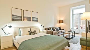 Um quarto moderno com uma cama grande, um sofá, uma escrivaninha e uma luminária. Há três quadros na parede e uma janela com persianas.