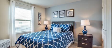 A bedroom with a large bed, two bedside tables with lamps, a bench, and three framed pictures on the wall.
