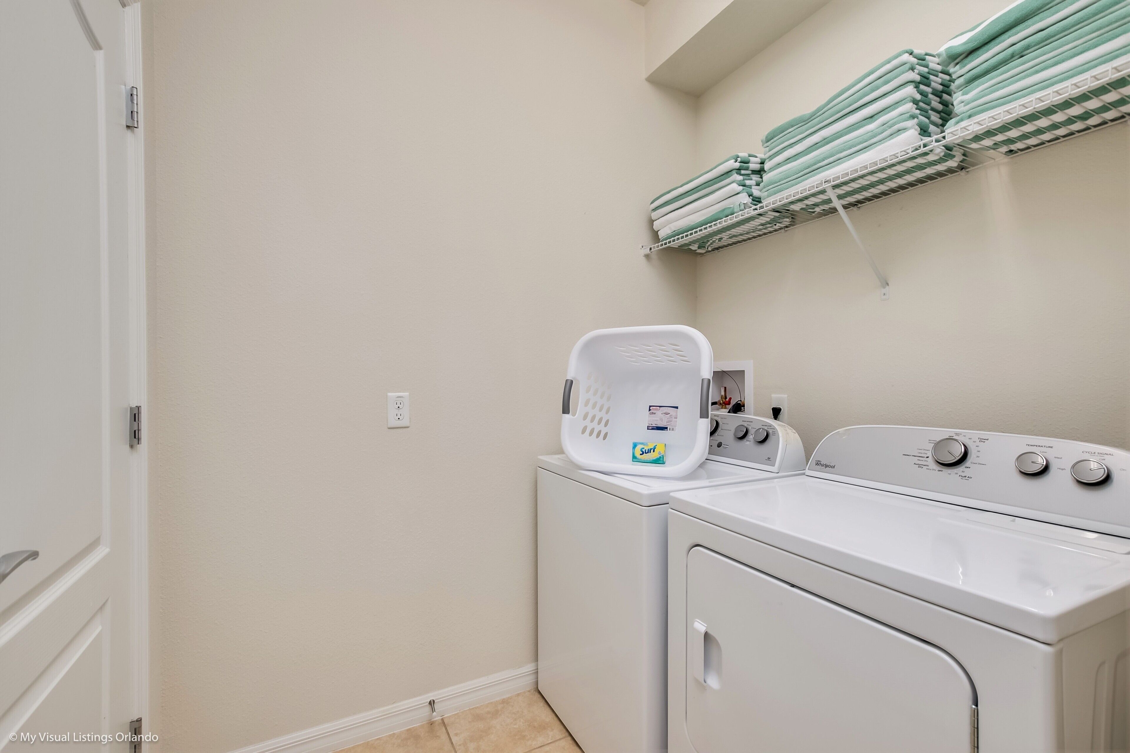 Un espace buanderie équipé d’un lave-linge et d’un sèche-linge à chargement frontal, d’un panier à linge empilable et d’une étagère où sont pliées les serviettes.