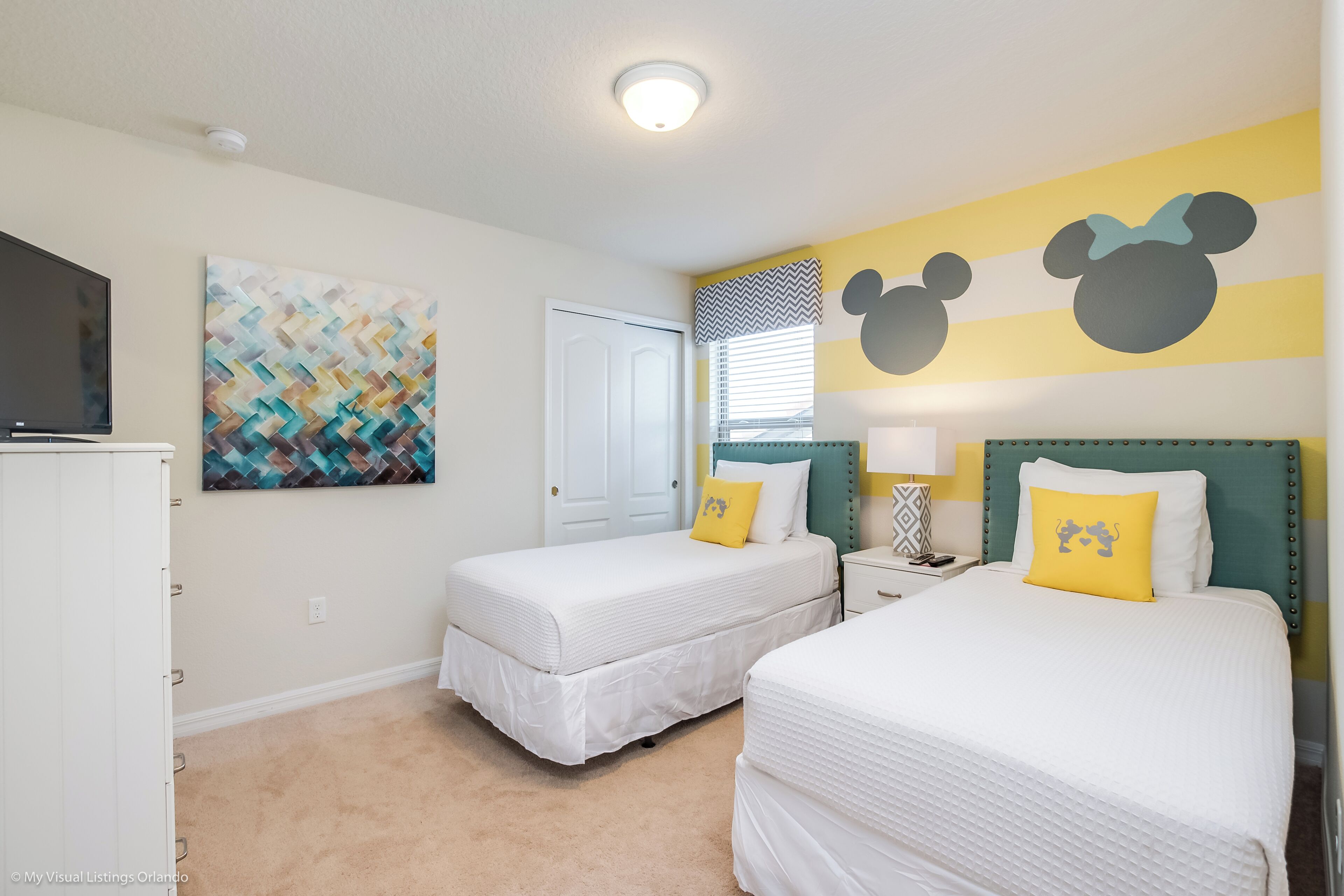 Ein Schlafzimmer mit zwei Betten, einem Fernseher, einem Gemälde und Wandstickern mit Mickey Mouse.