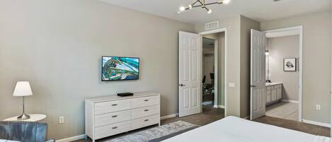 Une chambre à coucher comprenant un lit, une commode, un téléviseur et une porte donnant sur une autre pièce.