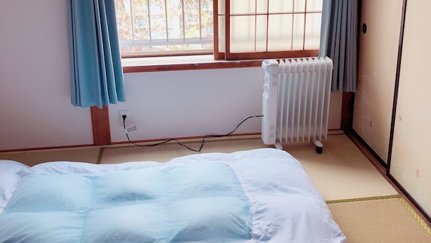 A room with a bed, a window with a view of greenery, a radiator, and a sliding door. - Guest House Ringo (Otaru)