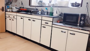 A kitchen with white cabinets, a microwave, and various kitchen items on the counter. - Guest House Ringo (Otaru)