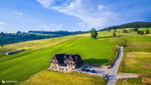 Un grand bâtiment à deux étages, doté d’un toit à forte pente, entouré de vastes champs verdoyants et surplombé d’un ciel dégagé.