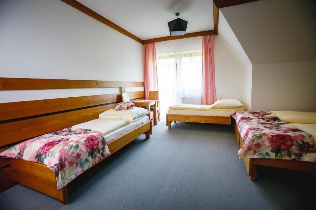 A room with two wooden beds, a small table, and a window with curtains.