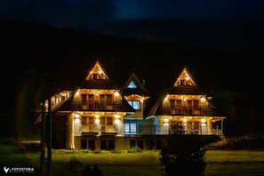 Ein großes, mehrstöckiges Holzhaus mit mehreren Balkonen und beleuchteter Fassade bei Nacht.