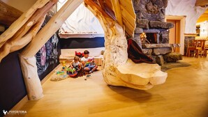 Une pièce chaleureuse avec un plafond en bois, une cheminée en pierre et un espace de jeux coloré pour les enfants.