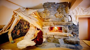 Une cheminée en pierre avec un feu, une table en bois ornée d’une affiche et un mur blanc.