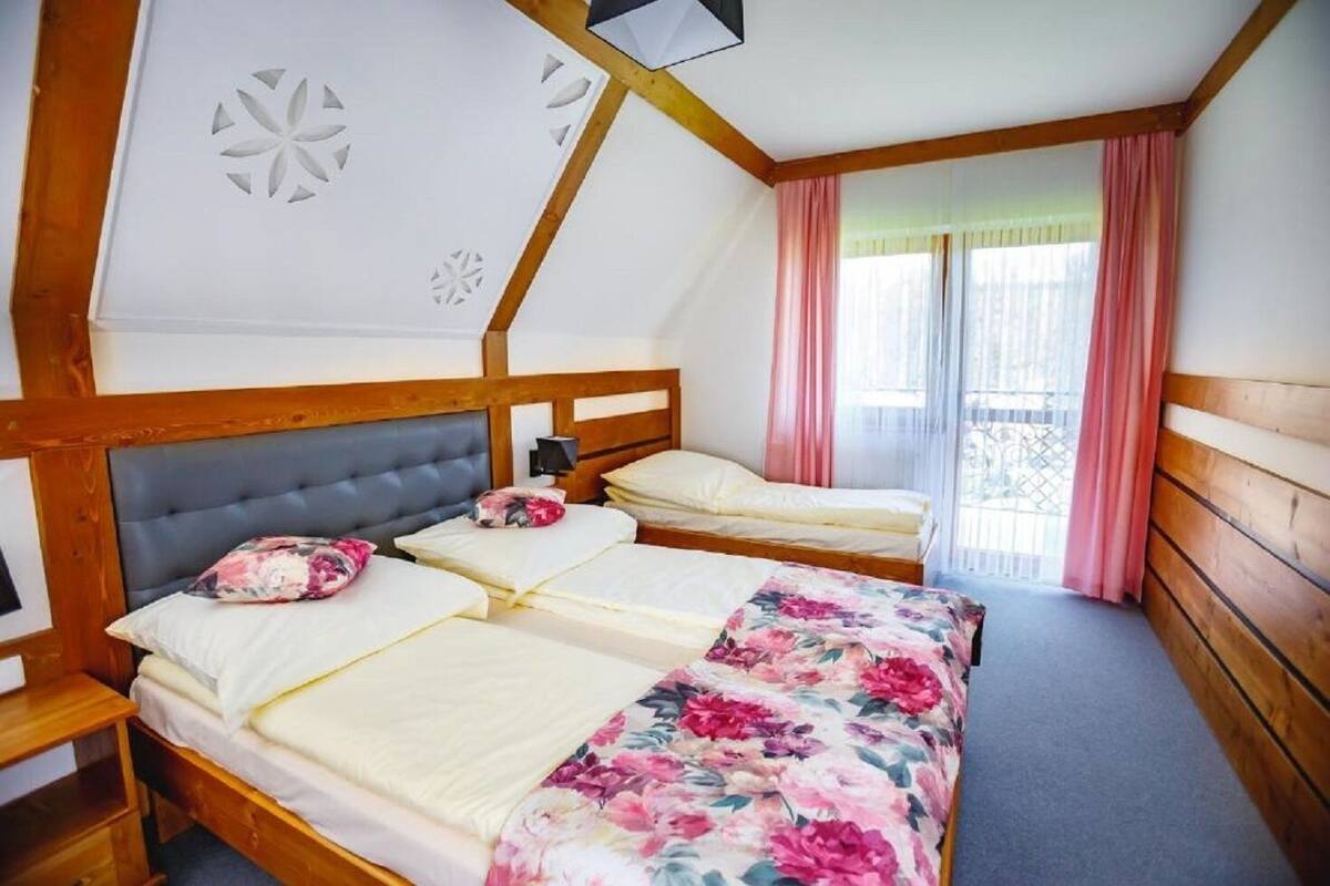 A room with two beds, wooden headboards, a nightstand, a lamp, and a window with pink curtains.