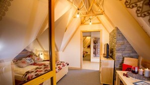 Une chambre mansardée chaleureuse, avec un lit, un bureau et un mur en pierre.