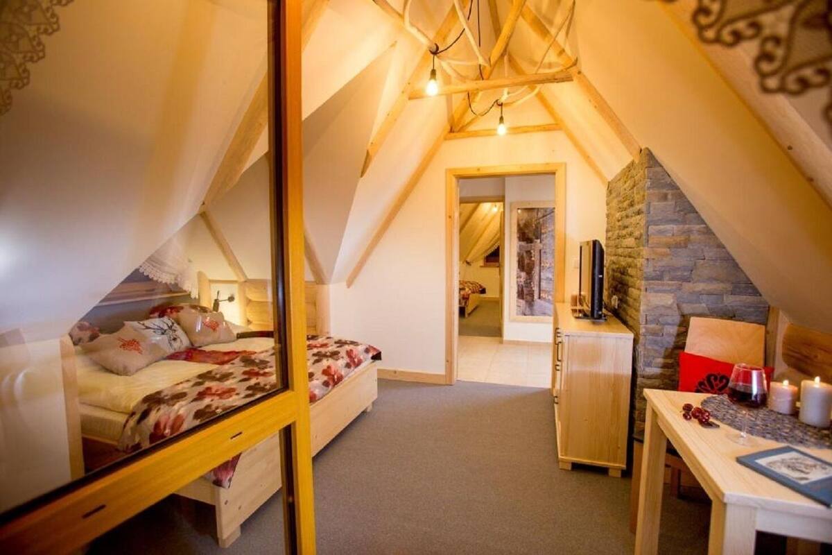 A cozy attic bedroom with a bed, a desk, and a stone wall.