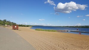 A beach with a paved walkway, wooden structures, and a dock extending into a lake. - Vacation home (110sqm) for rent at the Geiseltalsee (Krumpa)
