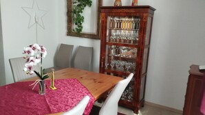 A dining area with a wooden table, white chairs, a pink tablecloth, a glass vase with flowers, a star decoration, a mirror, and a glass cabinet with wine glasses. - Vacation home (110sqm) for rent at the Geiseltalsee (Krumpa)