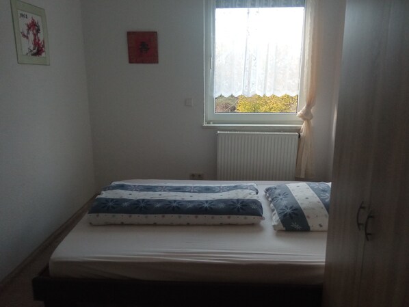 A small, sparsely furnished room with a single bed, a radiator, and a window with a view of trees.