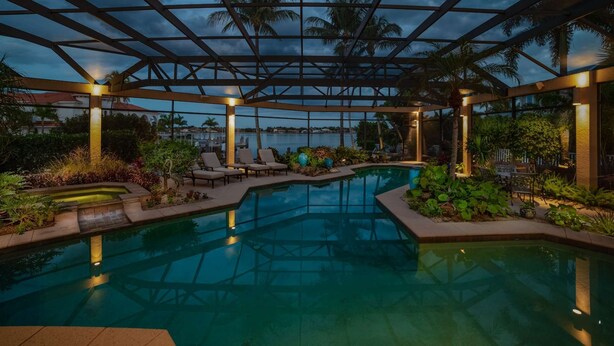 Piscina interna com teto de vidro, espreguiçadeiras e plantas tropicais.