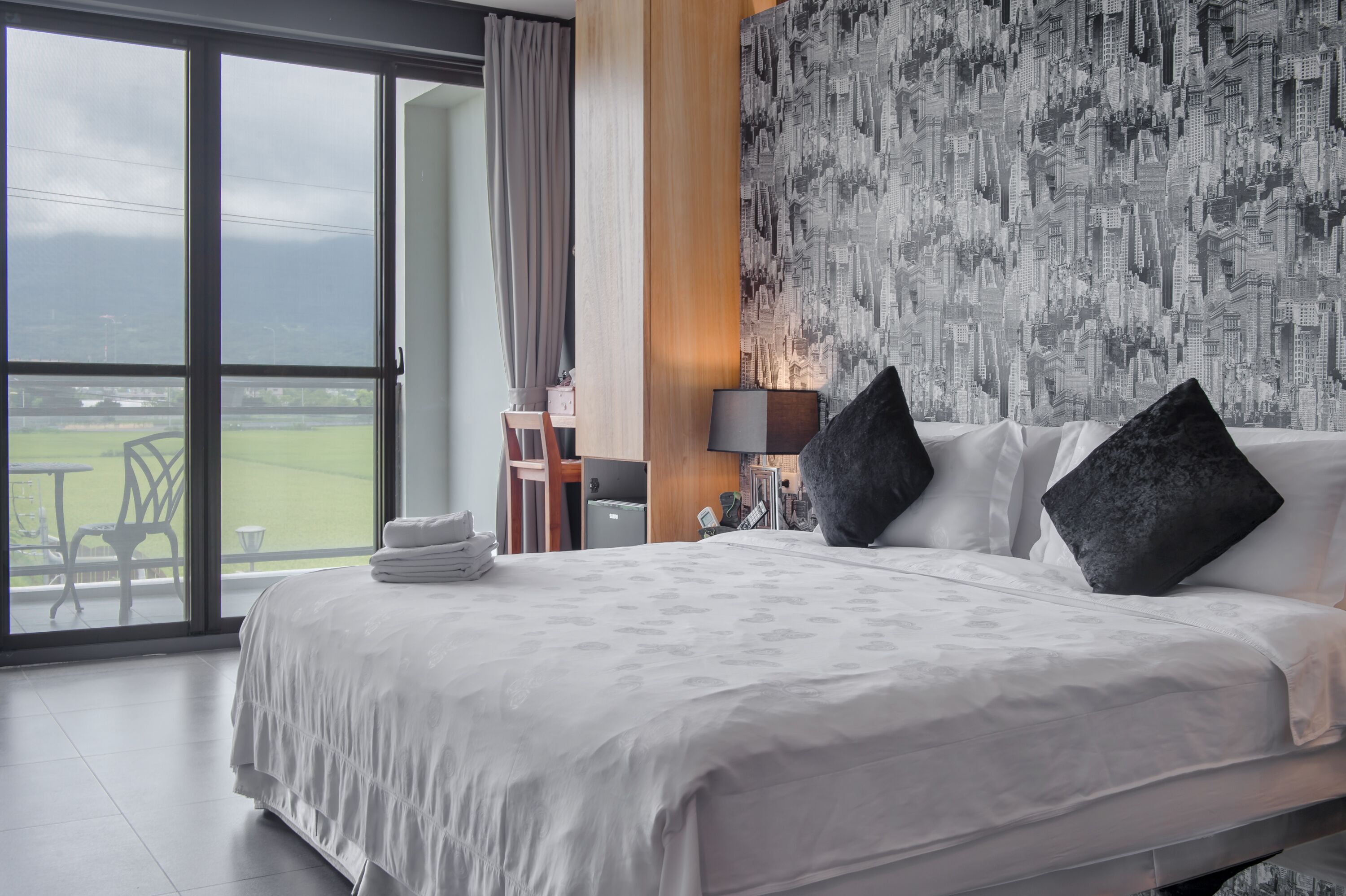A hotel room with a large bed, a cityscape wallpaper, and a view of a sports field.