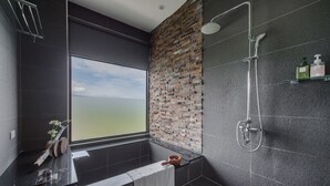 Een moderne badkamer met een groot raam, een accentmuur van baksteen, een douche en een wastafel met toiletartikelen.