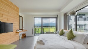 Een moderne hotelkamer met een groot bed, een aan de muur bevestigde televisie, een balkon met uitzicht op de stad en een houten accentmuur.