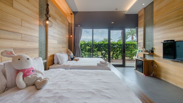 Een hotelkamer met twee bedden, een televisie, een klein kitchenette en een balkon met uitzicht op groen.