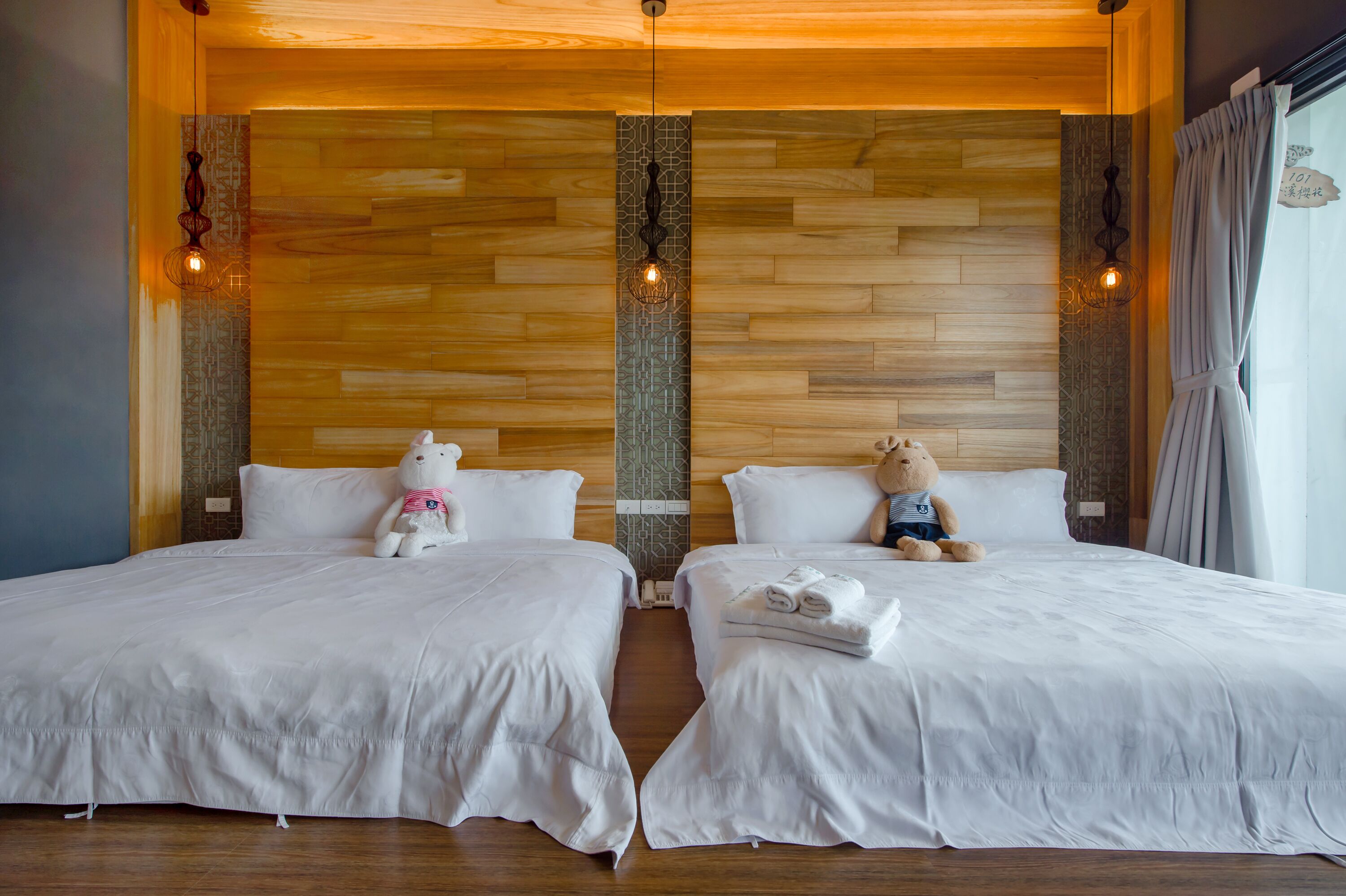 A hotel room with two beds, wooden panel walls, and decorative wall sconces.