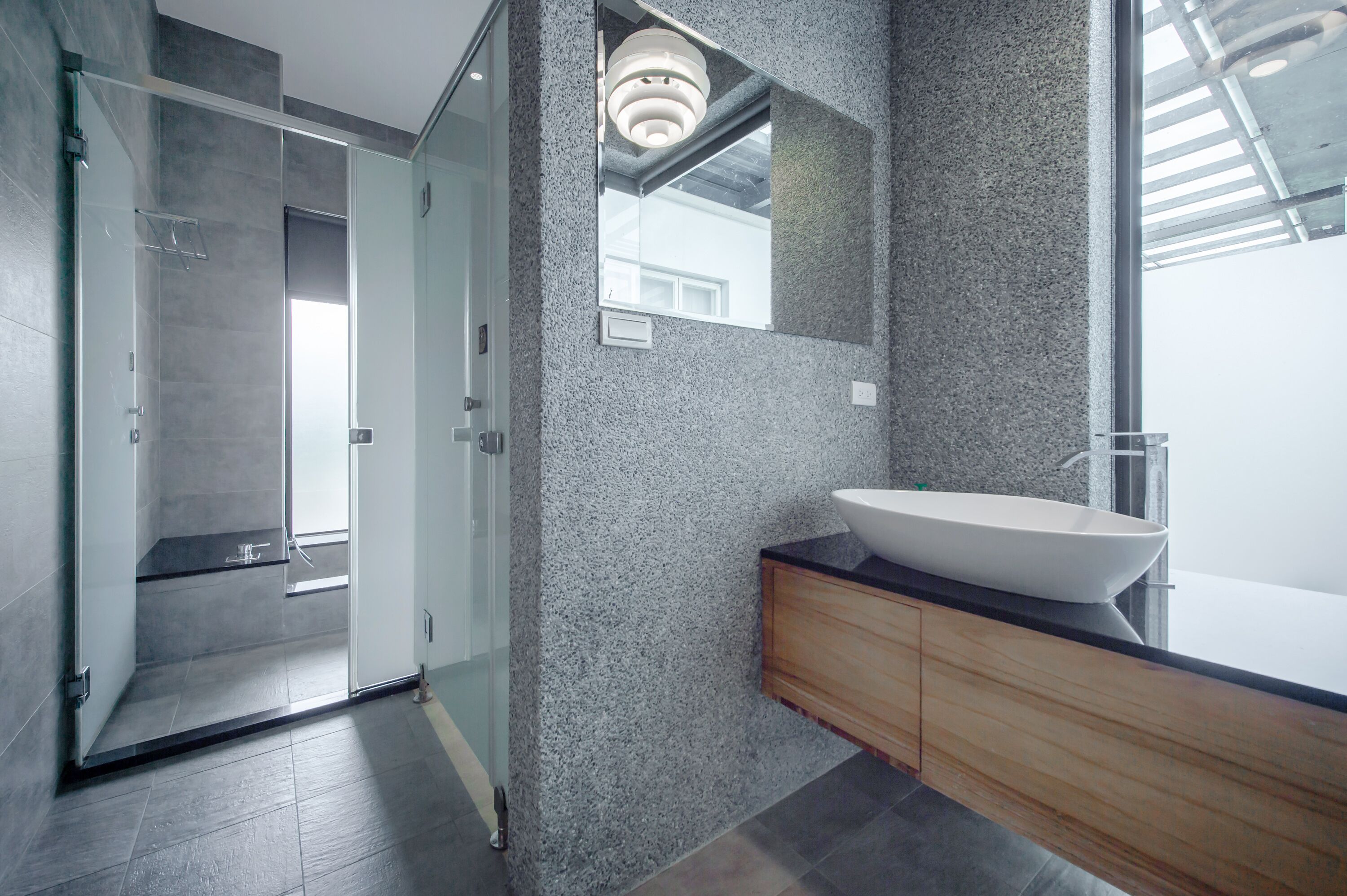 A modern bathroom with a glass shower enclosure, a large freestanding sink, and a wooden vanity.