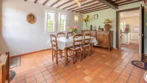 A dining area with a table set for four, wooden chairs, a cabinet, and a vase with flowers. - Charming cottage with enclosed garden in Green Picardy (Martincourt)