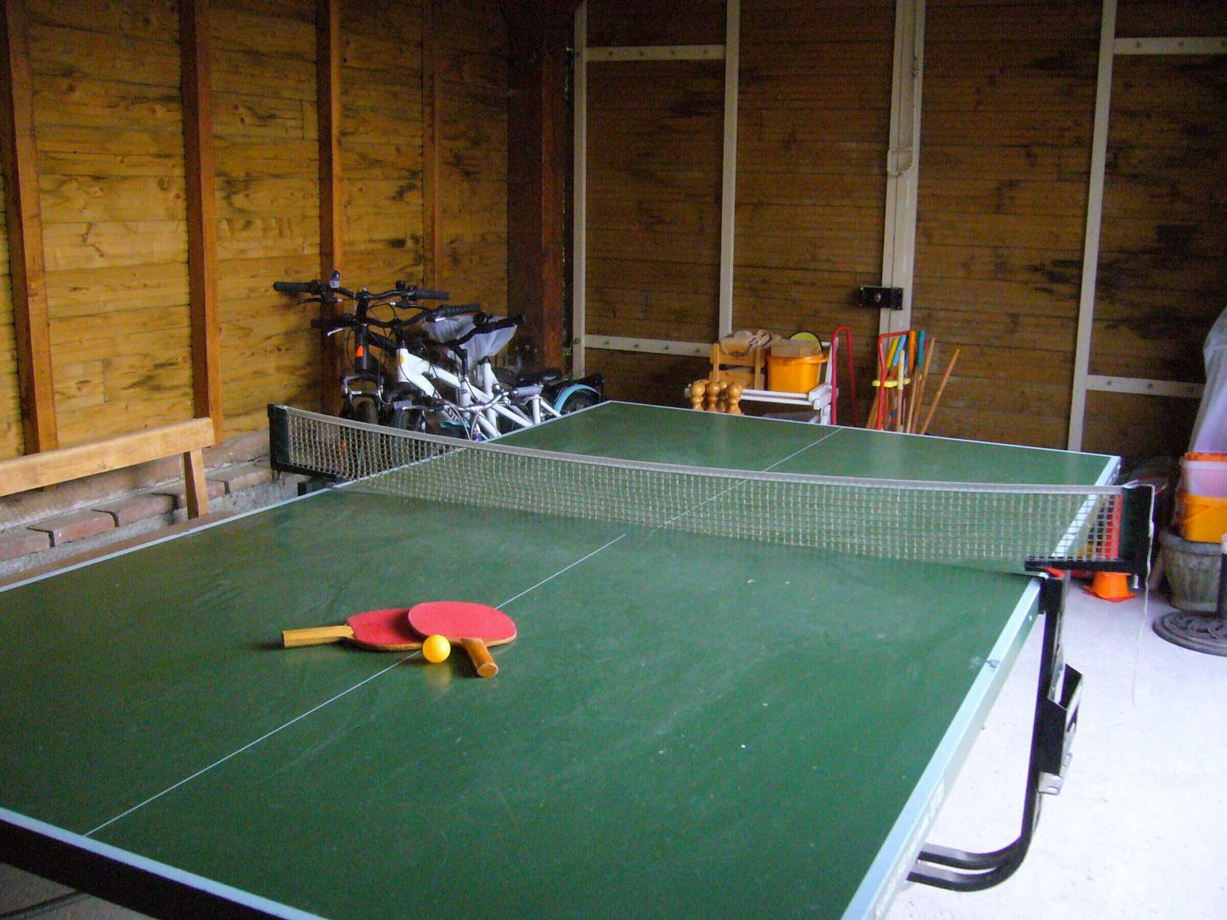 A ping pong table with paddles and a ball in a room with wooden walls and a bench.