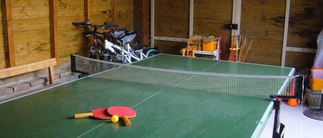 A ping pong table with paddles and a ball in a room with wooden walls and a bench.