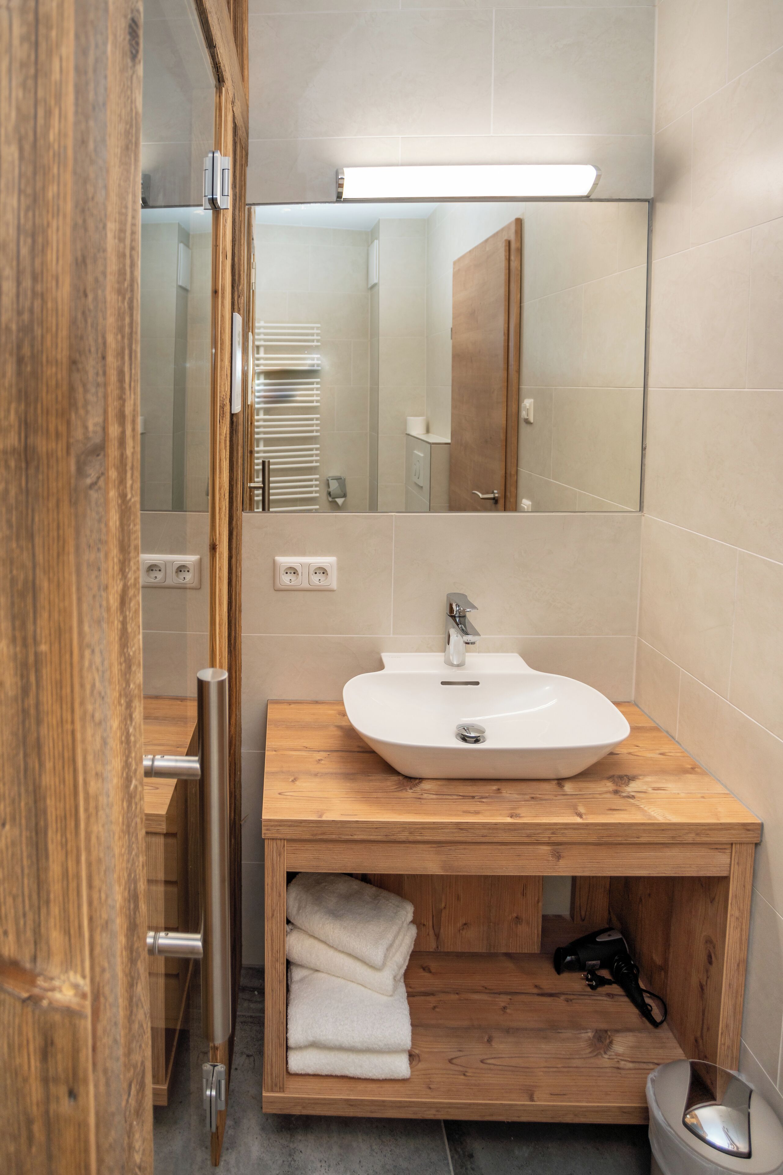 A modern bathroom with a wooden vanity, a white sink, a mirror, and a towel rack.
