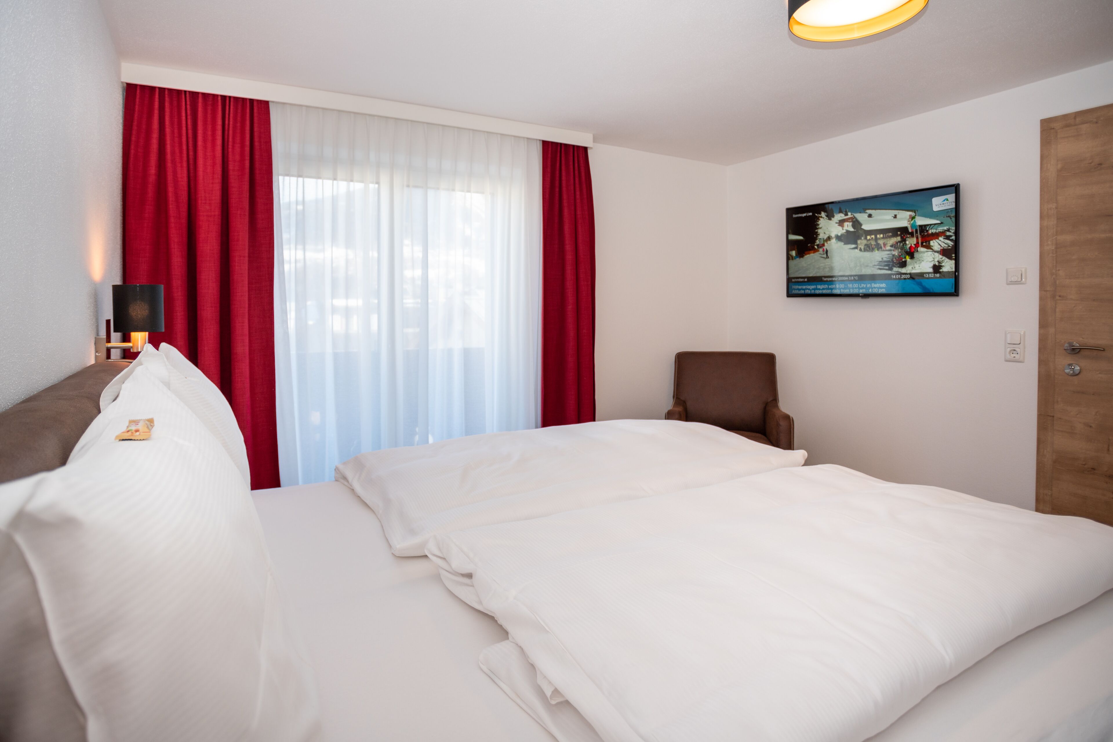 A hotel room with a bed, a chair, a TV, and a window with curtains.