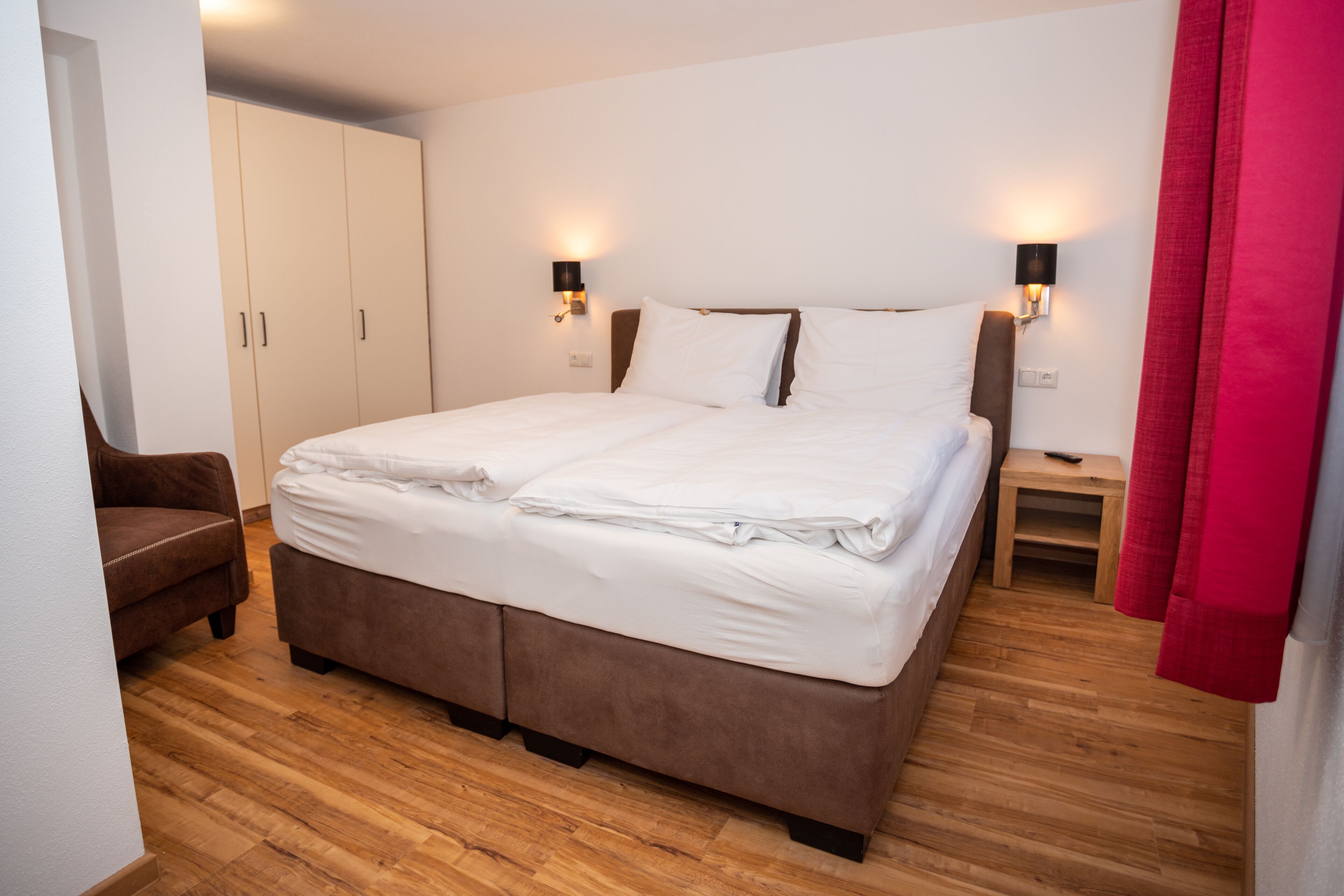 Een slaapkamer met een bed, houten vloeren, een kledingkast en twee nachtkastjes met lampen.