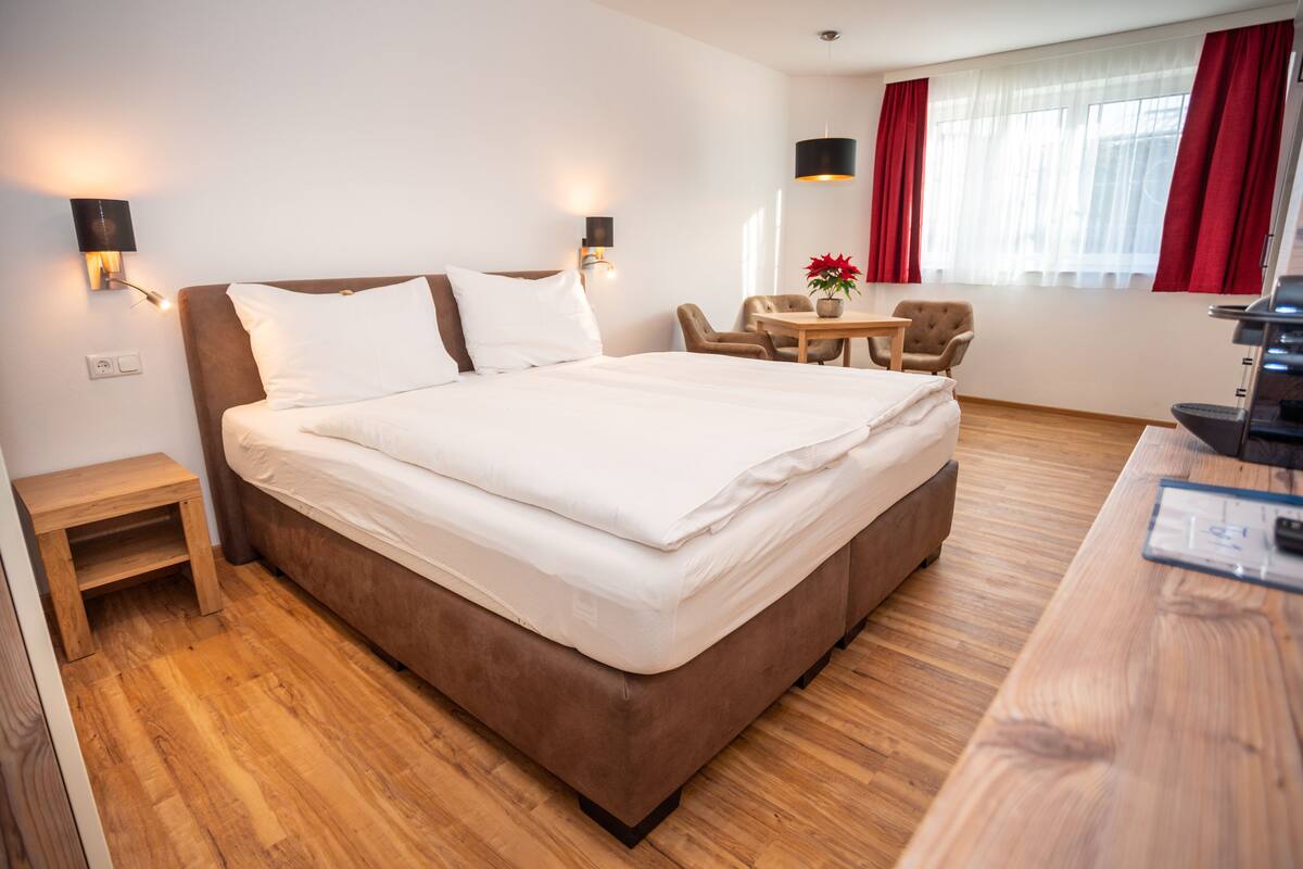 A modern hotel room with a large bed, a wooden desk, a small table, and two chairs.