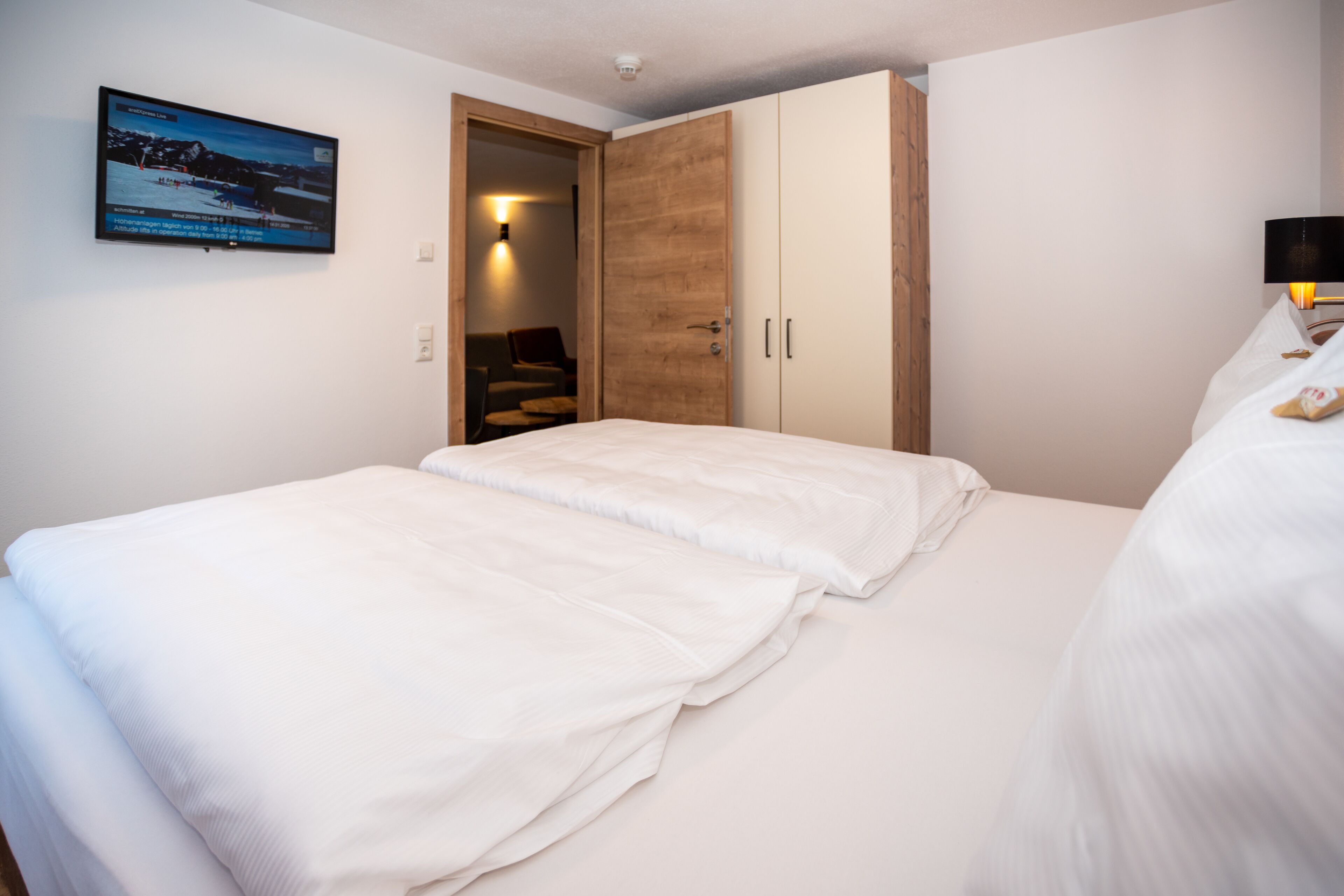 Un dormitorio con cama, armario, televisor montado en la pared y puerta que da a otra habitación.