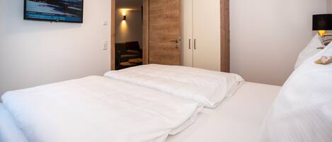 Un dormitorio con cama, armario, televisor montado en la pared y puerta que da a otra habitación.