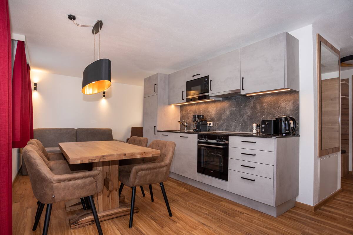 A modern kitchen with a dining area, featuring a wooden table and chairs, a built-in oven, and a microwave.