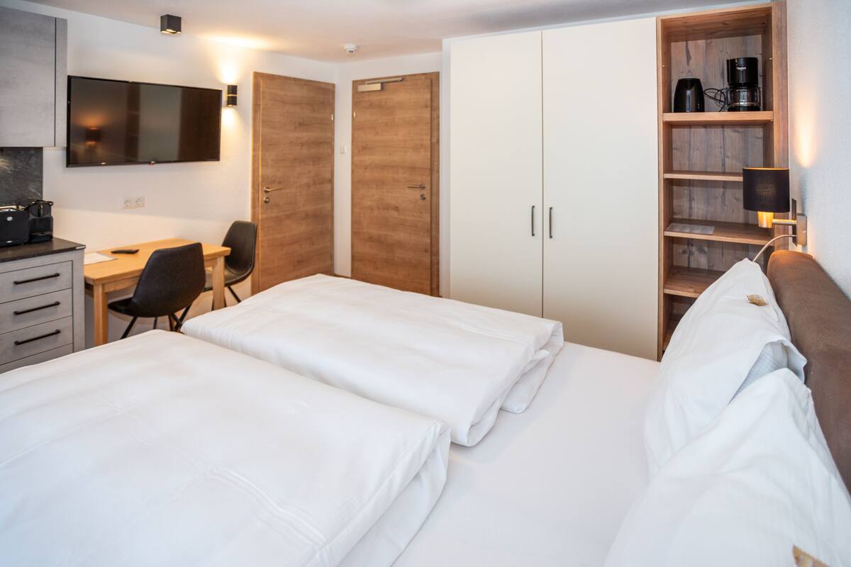 A hotel room with two beds, a desk, a chair, a TV, and a wardrobe.
