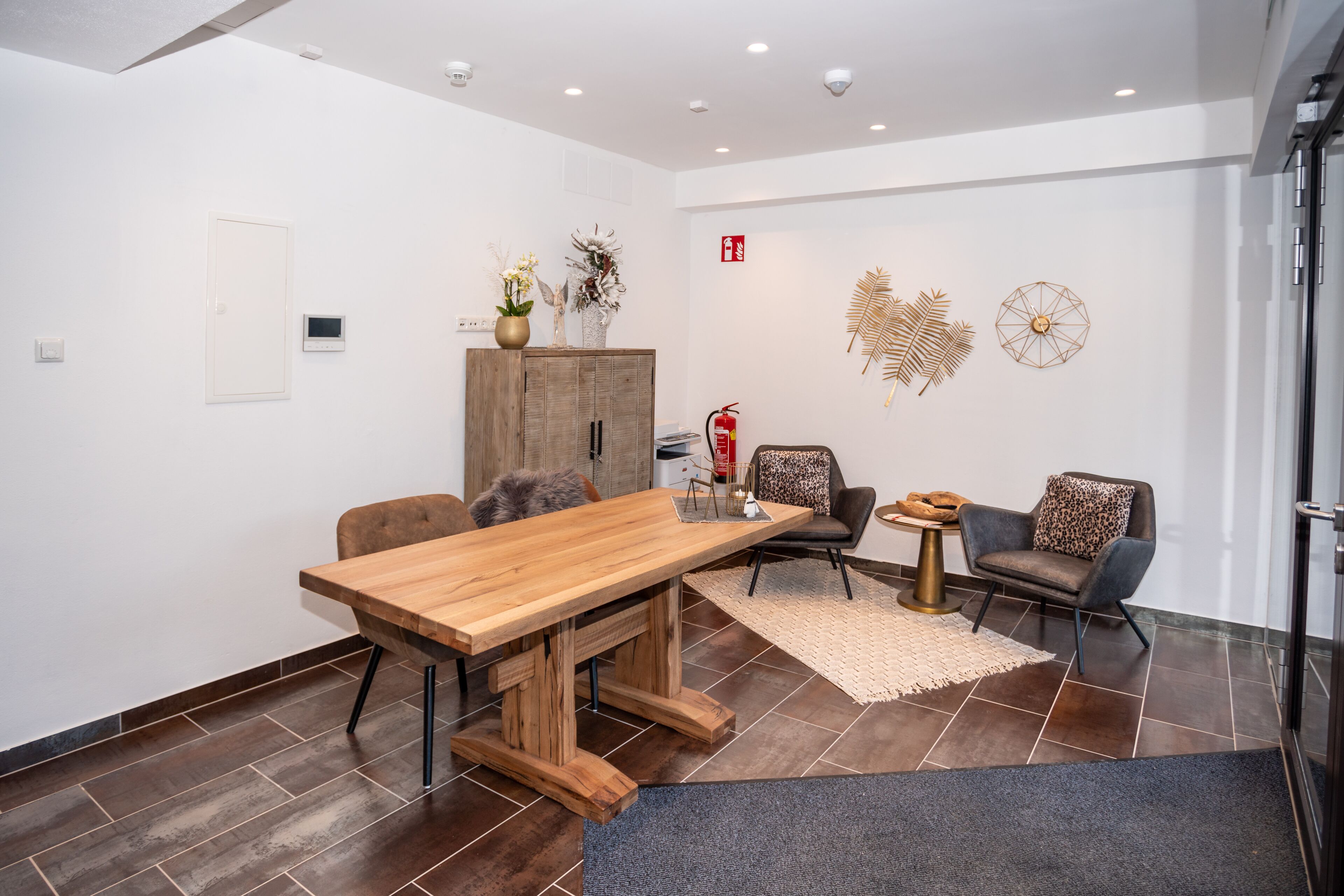 Una sala de reuniones moderna con una mesa de madera, dos sillas, un mueble decorativo y obras de arte en la pared.