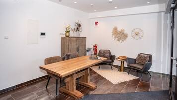 A modern meeting room with a wooden table, two chairs, a decorative cabinet, and wall art.
