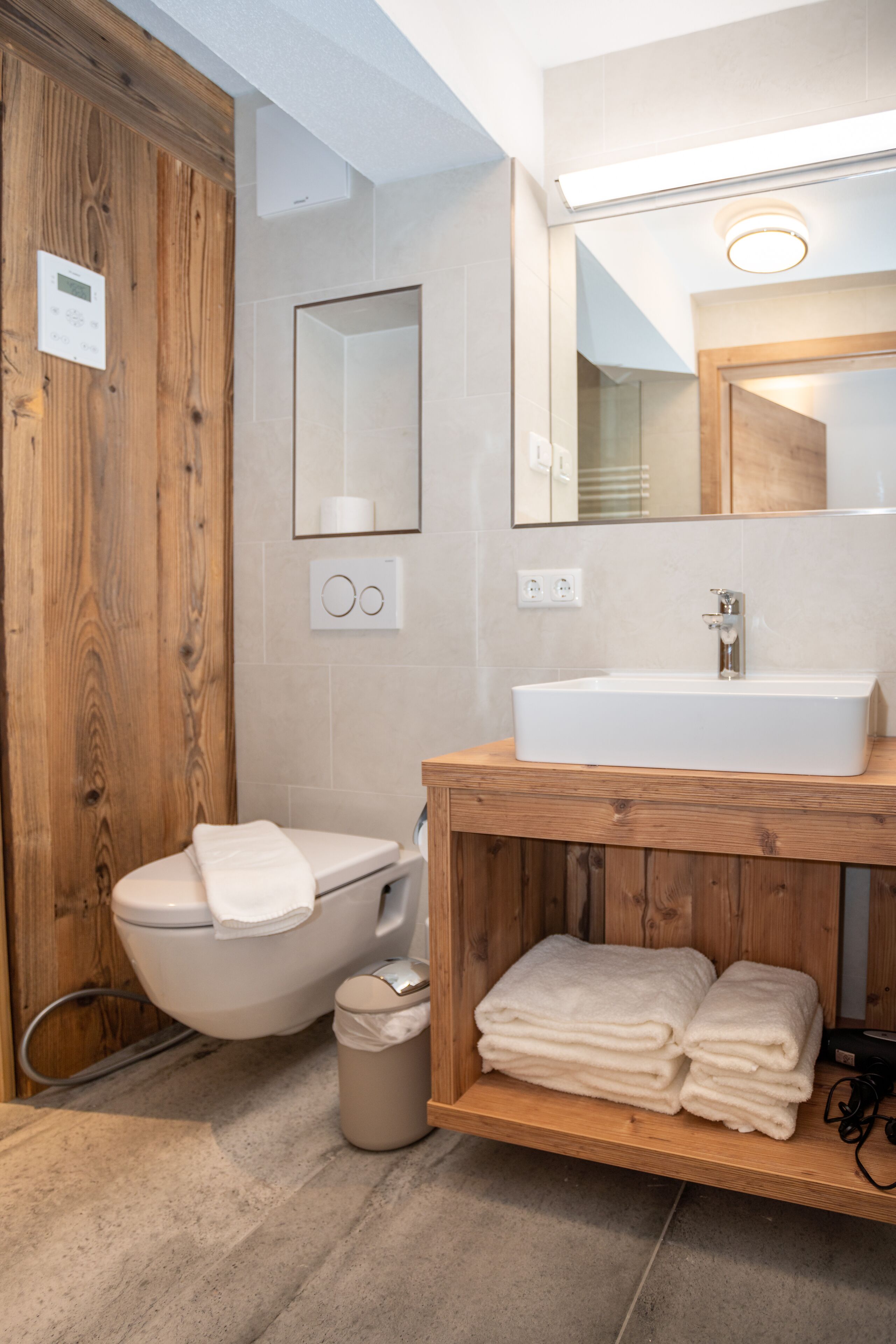 A modern bathroom with a wooden vanity, a white sink, and a toilet.