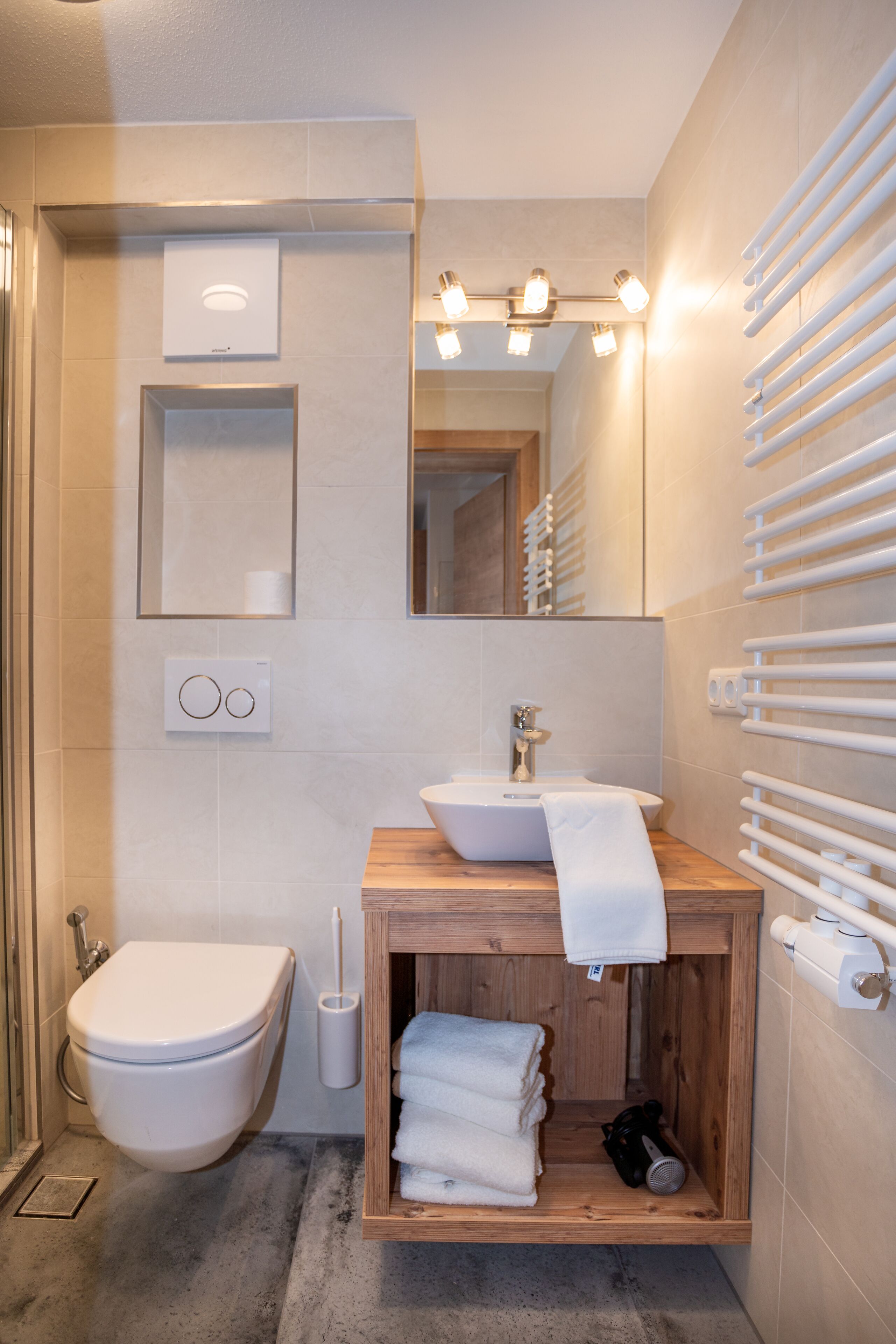 A modern bathroom with a wooden vanity, a white sink, a toilet, and a towel rack.