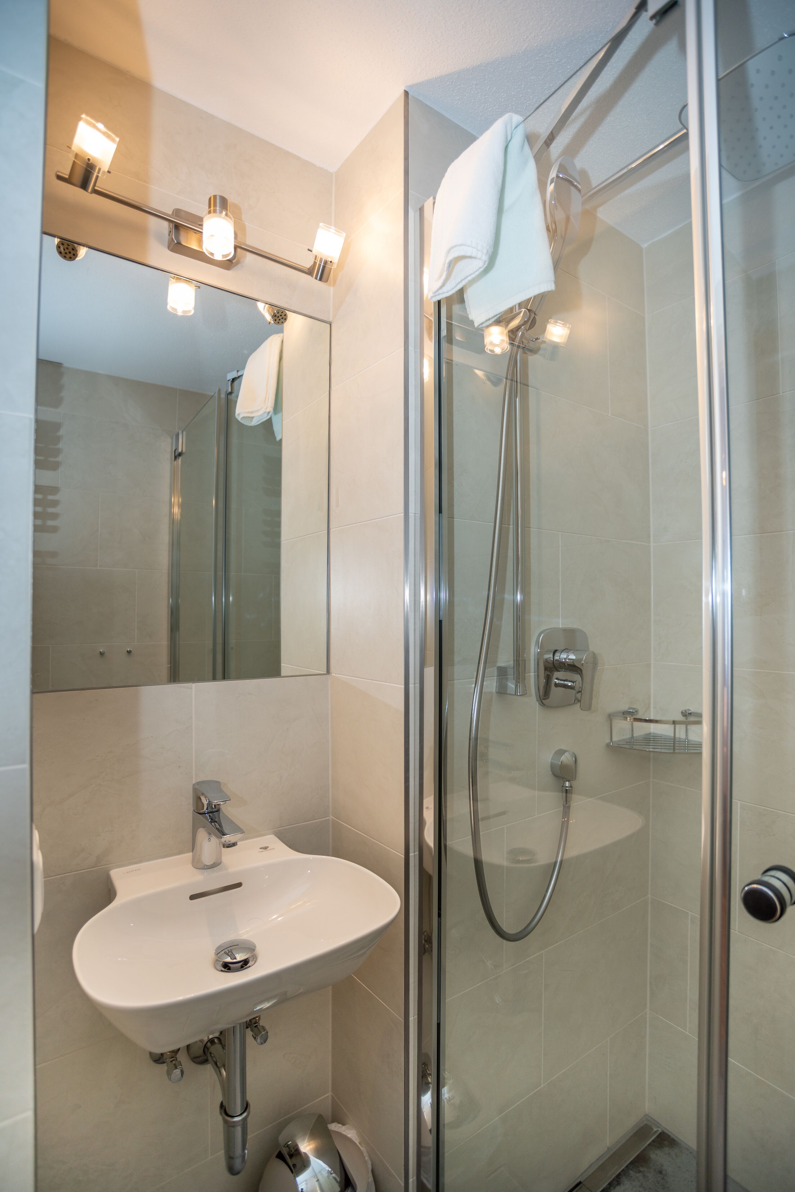 Un baño moderno con ducha de vidrio, lavamanos blanco y espejo con luces.
