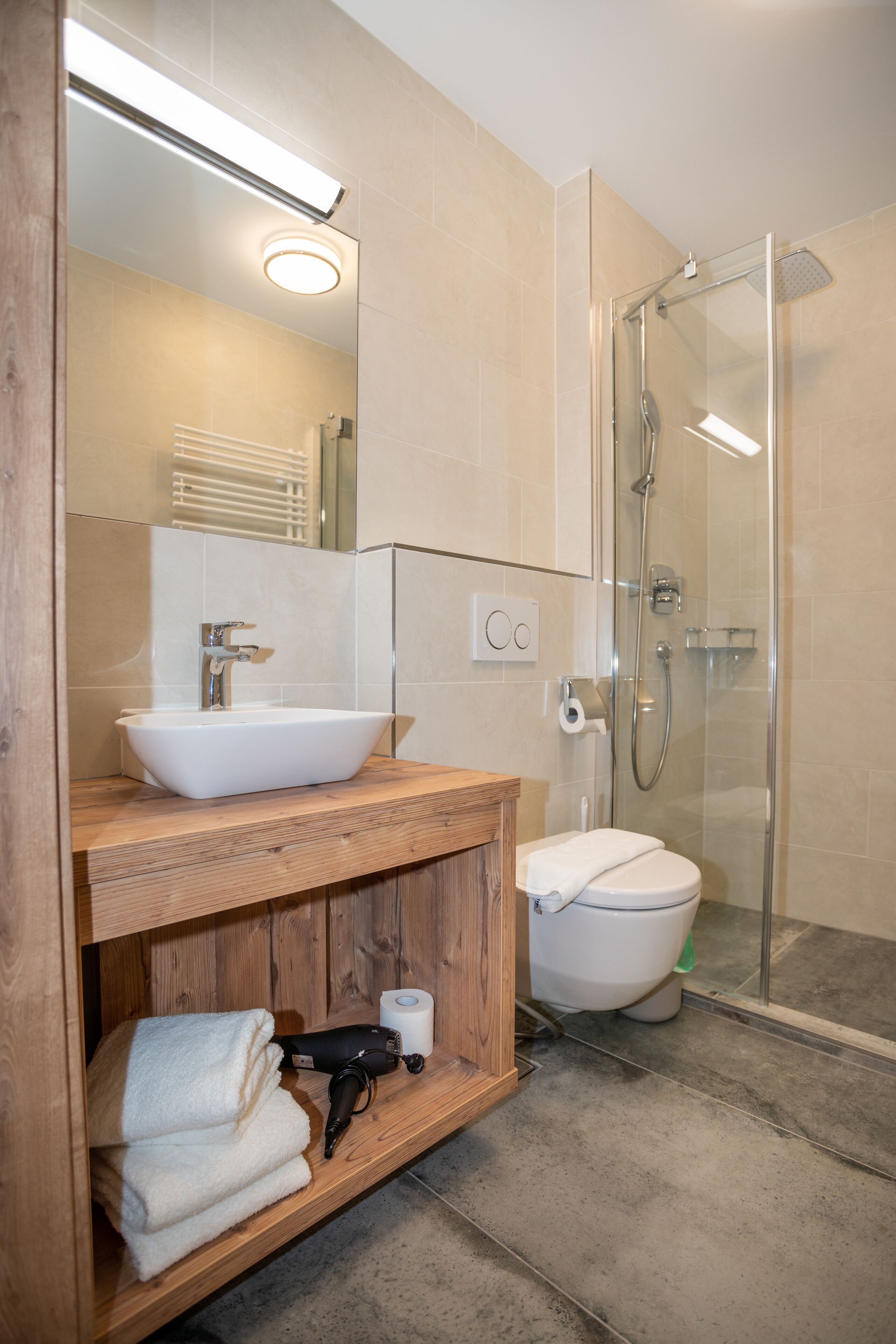 Ein modernes Badezimmer mit Waschtisch aus Holz, einem weißen Waschbecken, einer Glasdusche und einer Toilette.