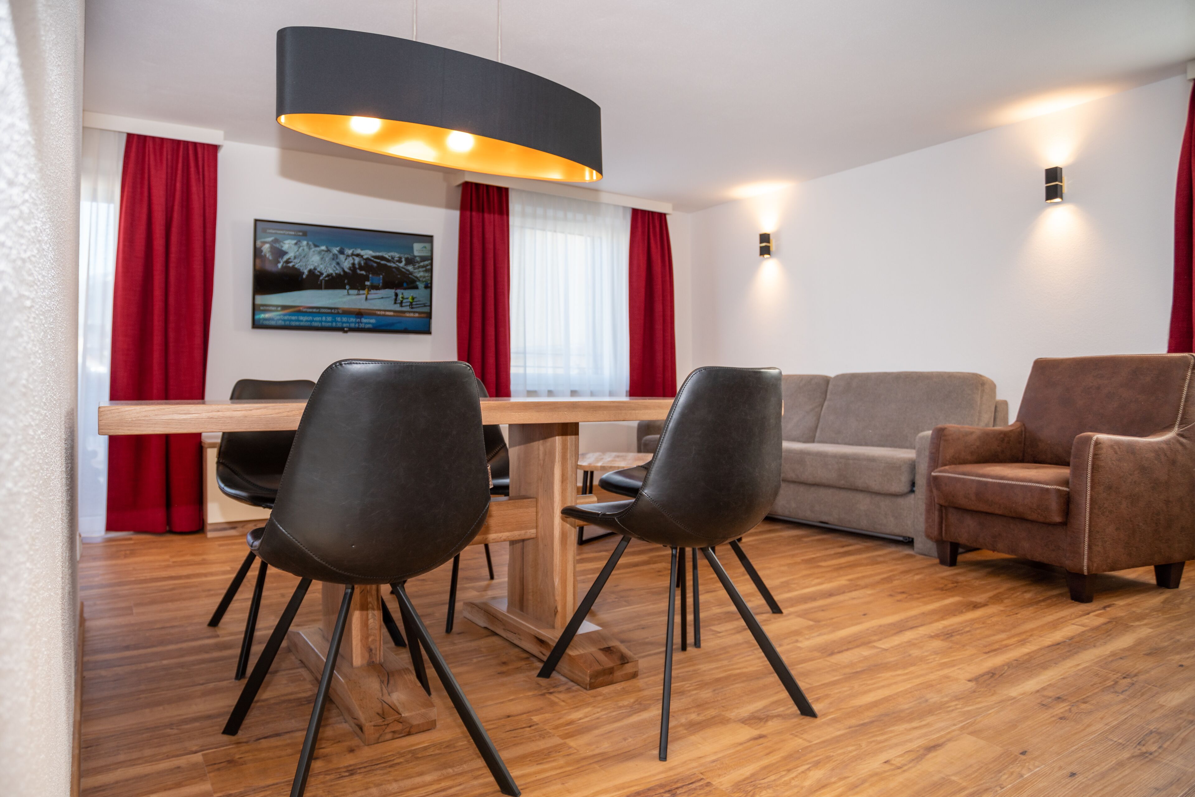 Una sala de estar moderna con una mesa de comedor de madera, sillas negras, un sofá gris y un sillón marrón.