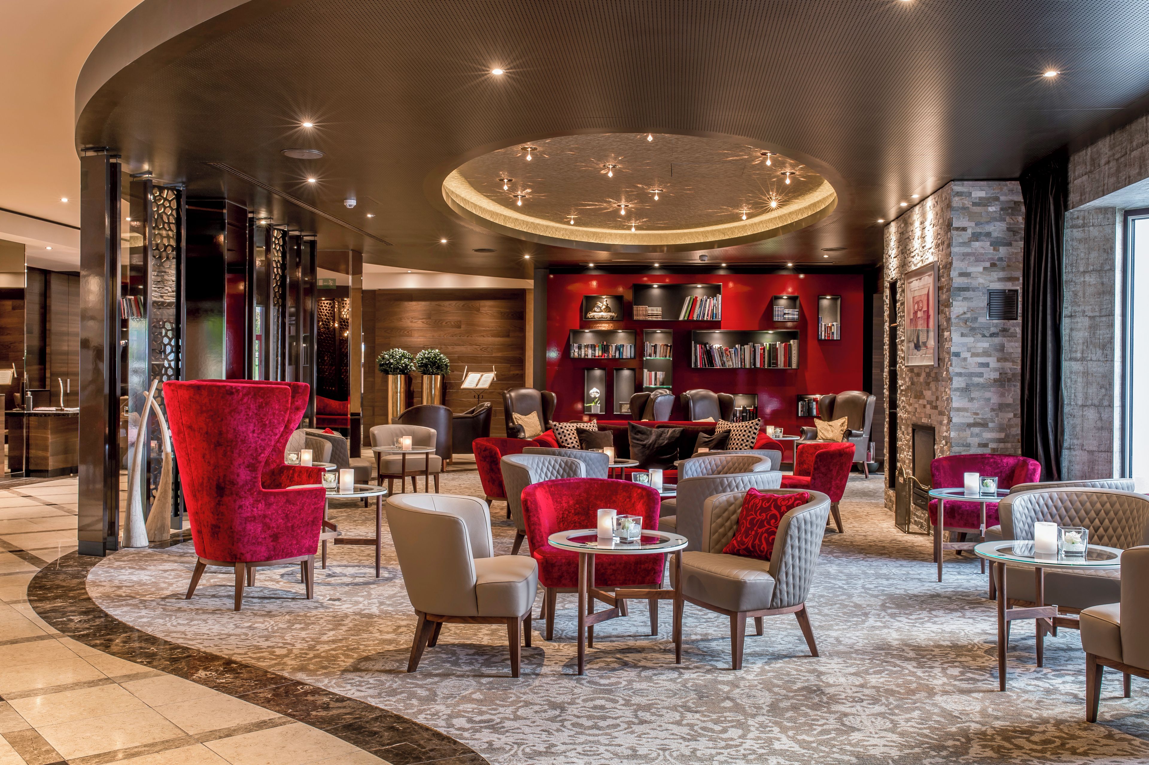 A modern lounge area with leather seating, a red wall with bookshelves, and a circular ceiling light fixture.