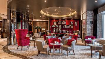 A modern lounge area with leather seating, a red wall with bookshelves, and a circular ceiling light fixture.