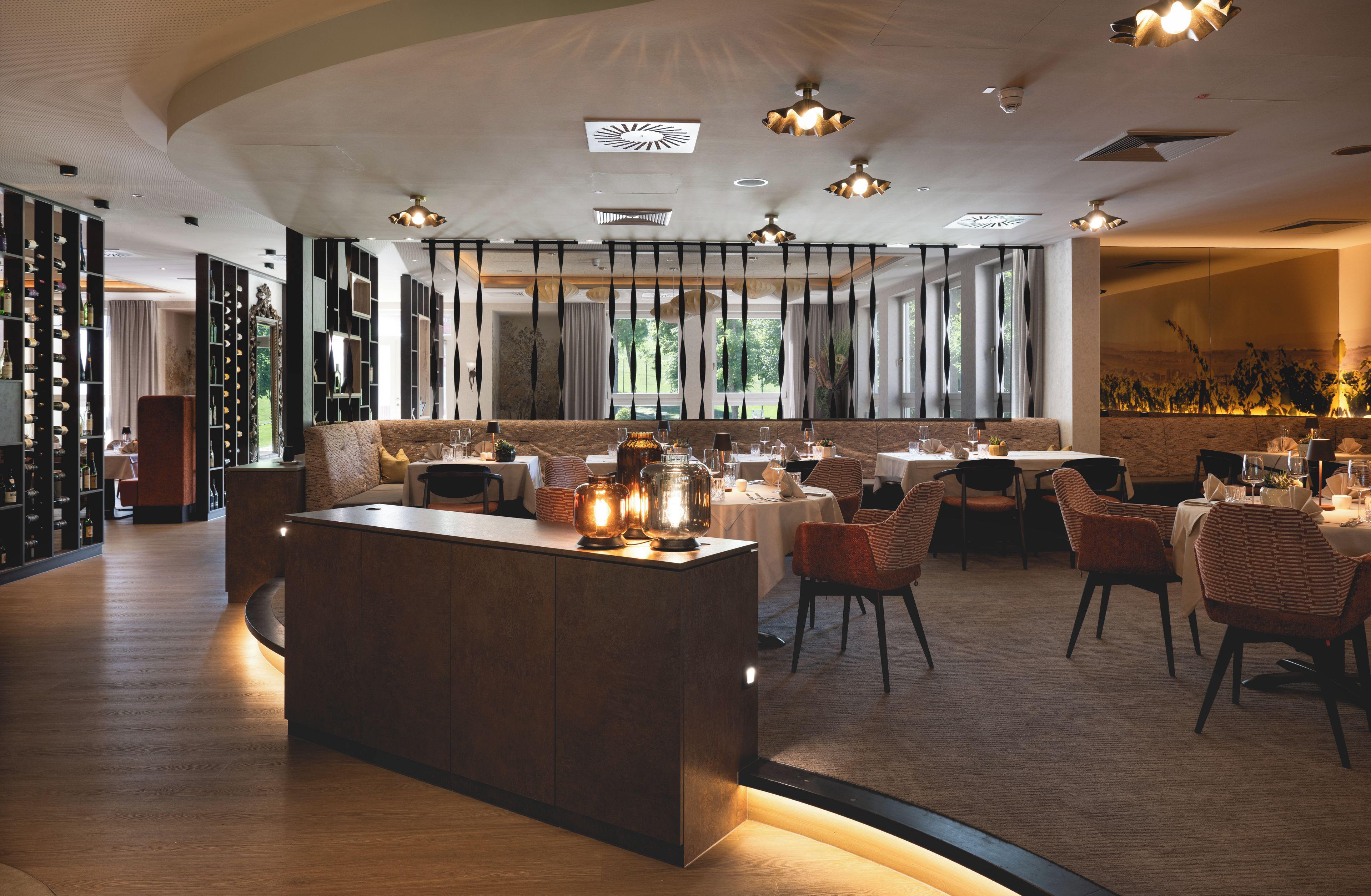 Ein modernes Restaurant-Interieur mit einer zentralen Kochinsel, Esstischen und Stühlen.