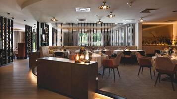 Ein modernes Restaurant-Interieur mit einer zentralen Kochinsel, Esstischen und Stühlen.