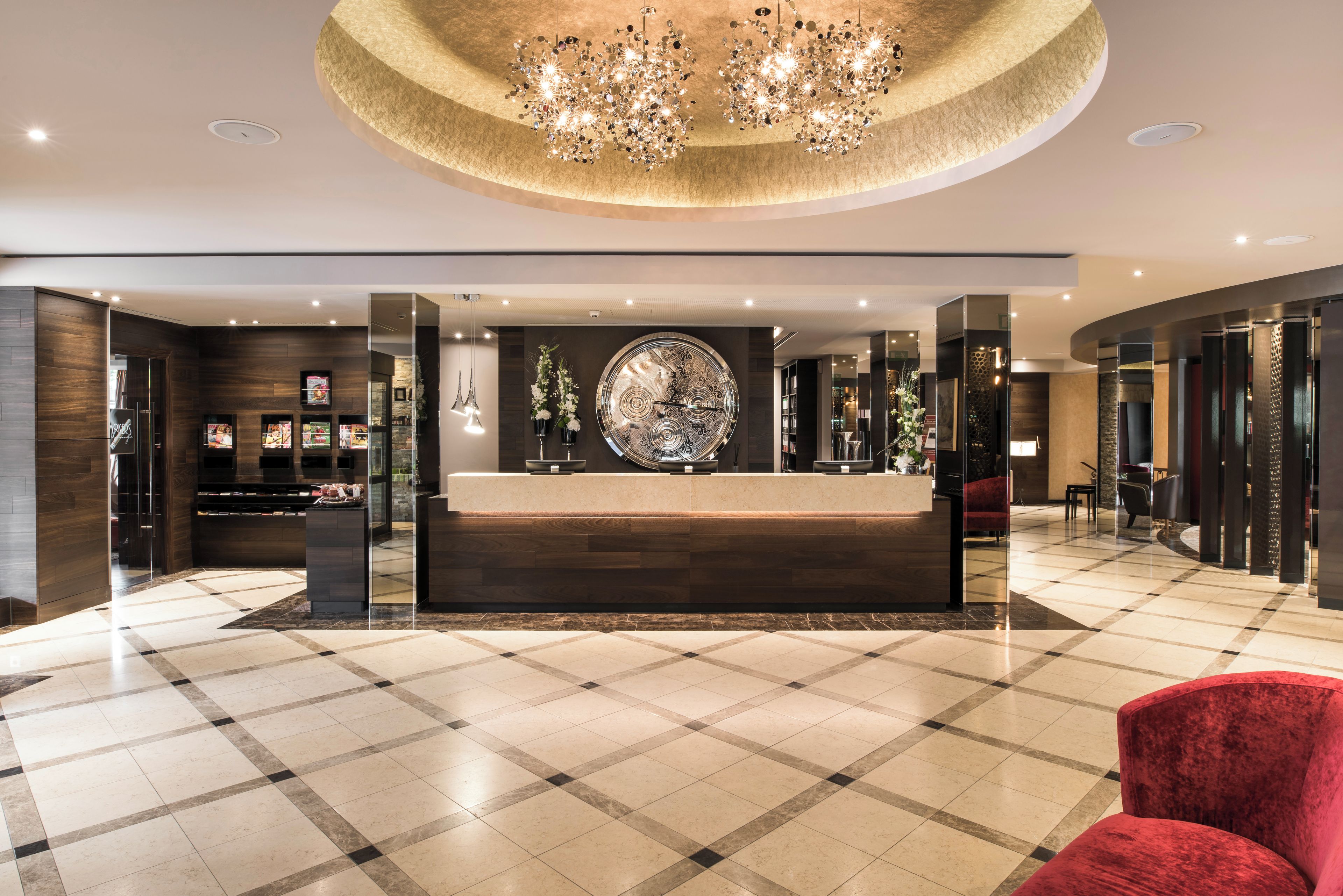 A hotel lobby with a reception desk, a large decorative clock, and a chandelier.